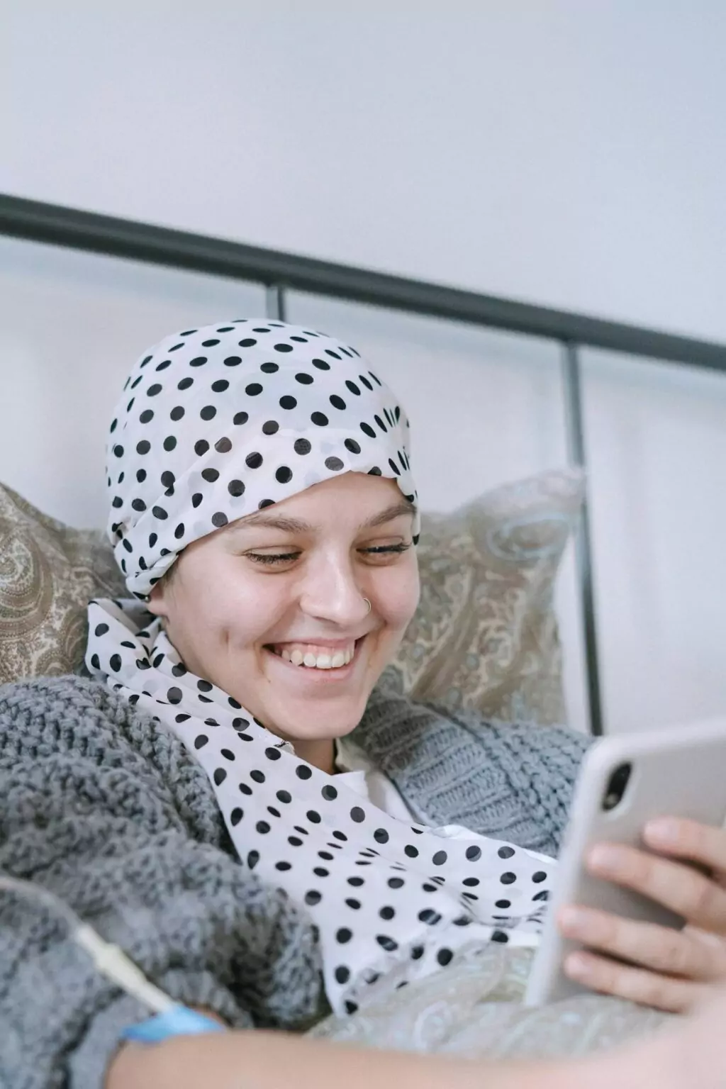 Femme souriante portant un foulard à pois et consultant son smartphone à domicile.
