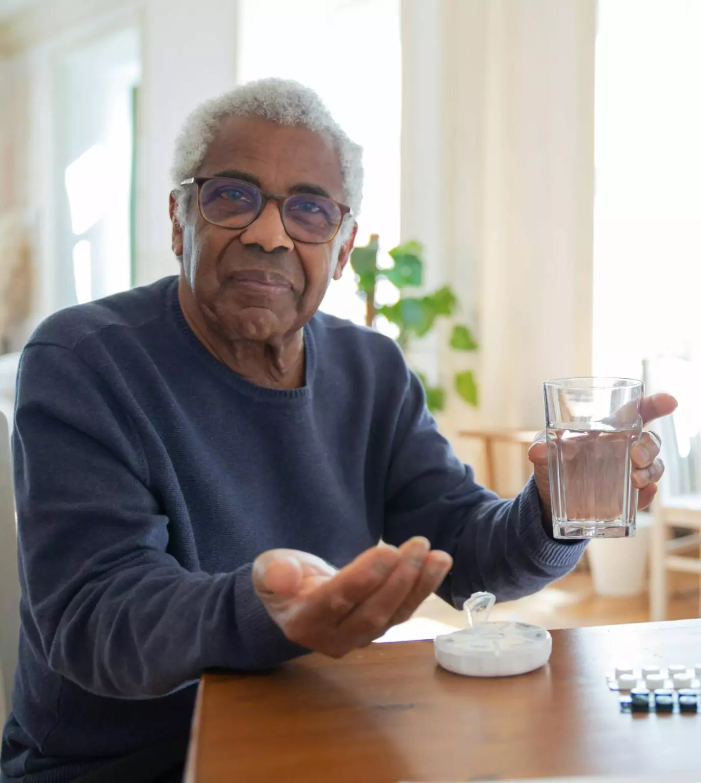 Homme âgé tenant un verre d’eau et préparant la prise de ses médicaments à domicile.